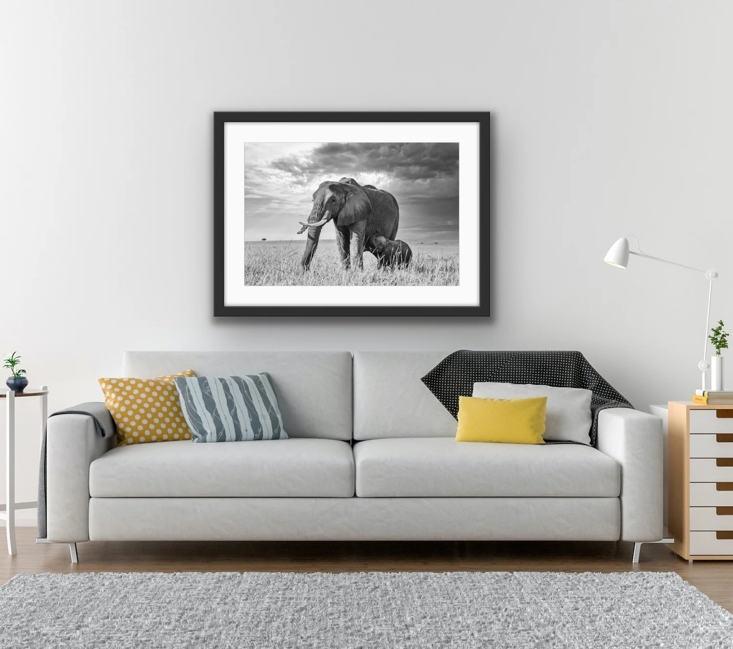 Framed elephant and calf photograph above a pale sofa with yellow cushions