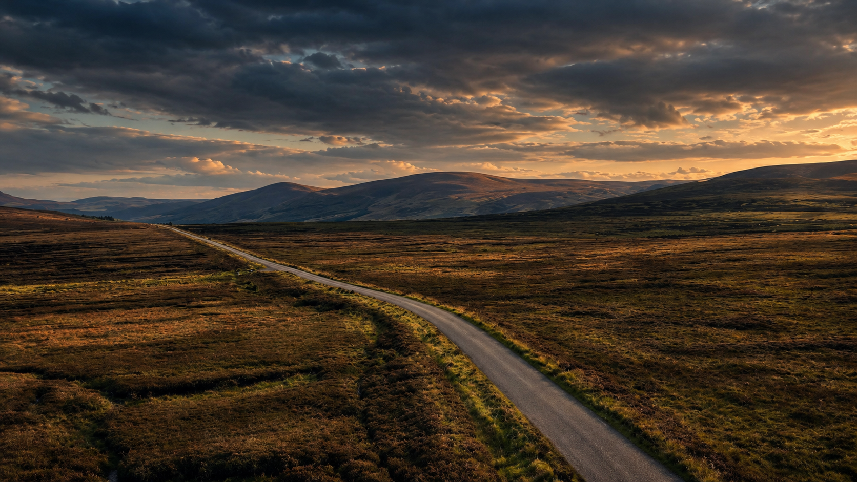 A winding road across open moorland beneath a sunset sky