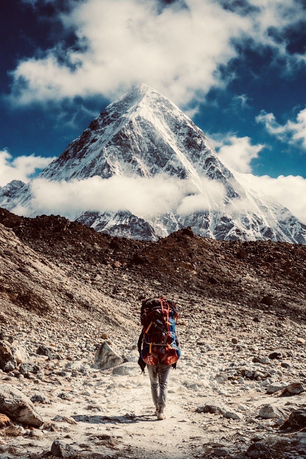A hiker with a red backpack beneath a towering snowy peak