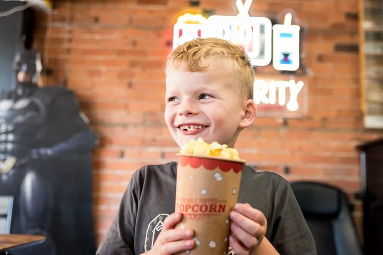 A young guest grinning with a cup of freshly popped POPularity! popcorn