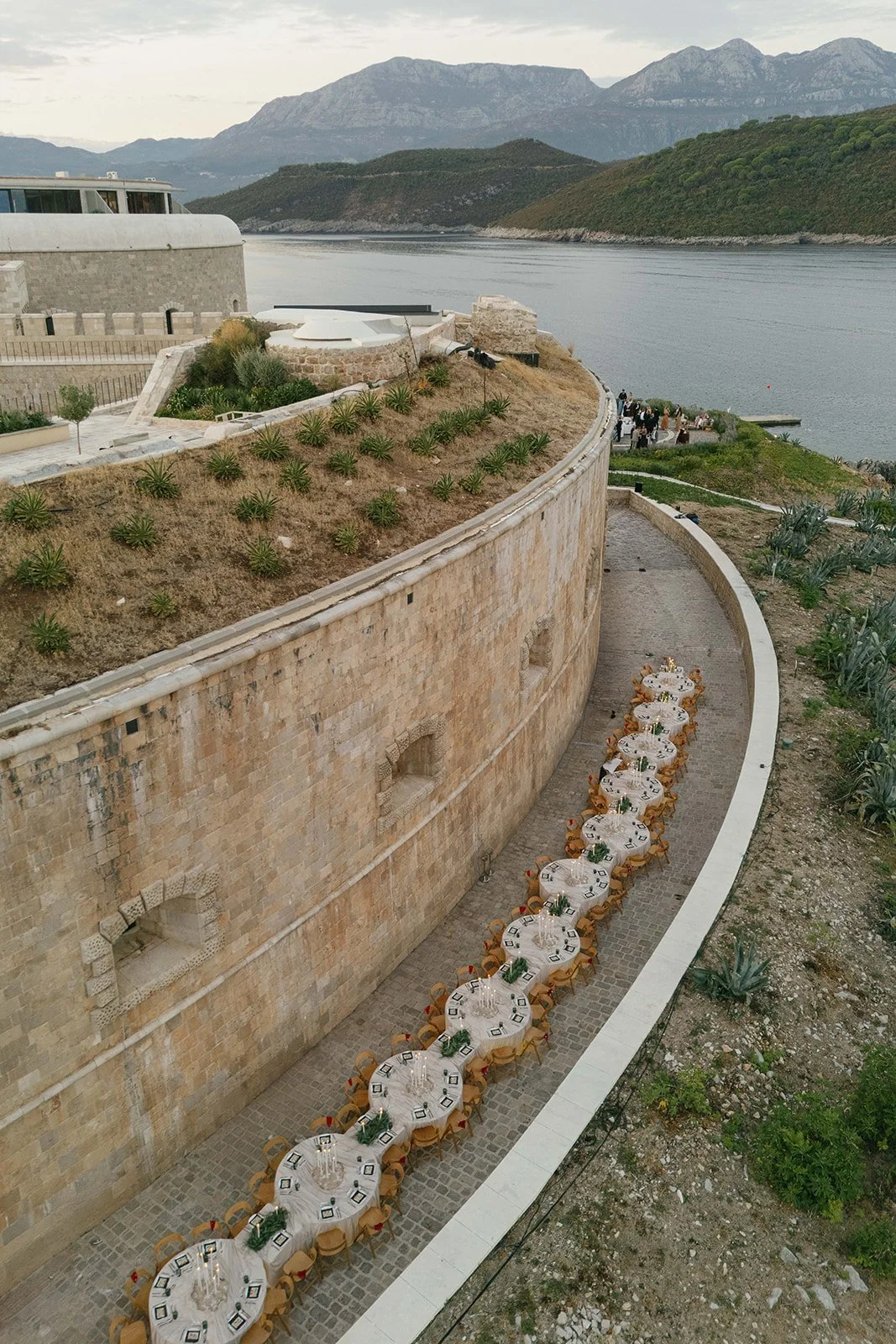 Aerial drone view of serpentine long dinner table setup along the stone fortress path on Mamula Island