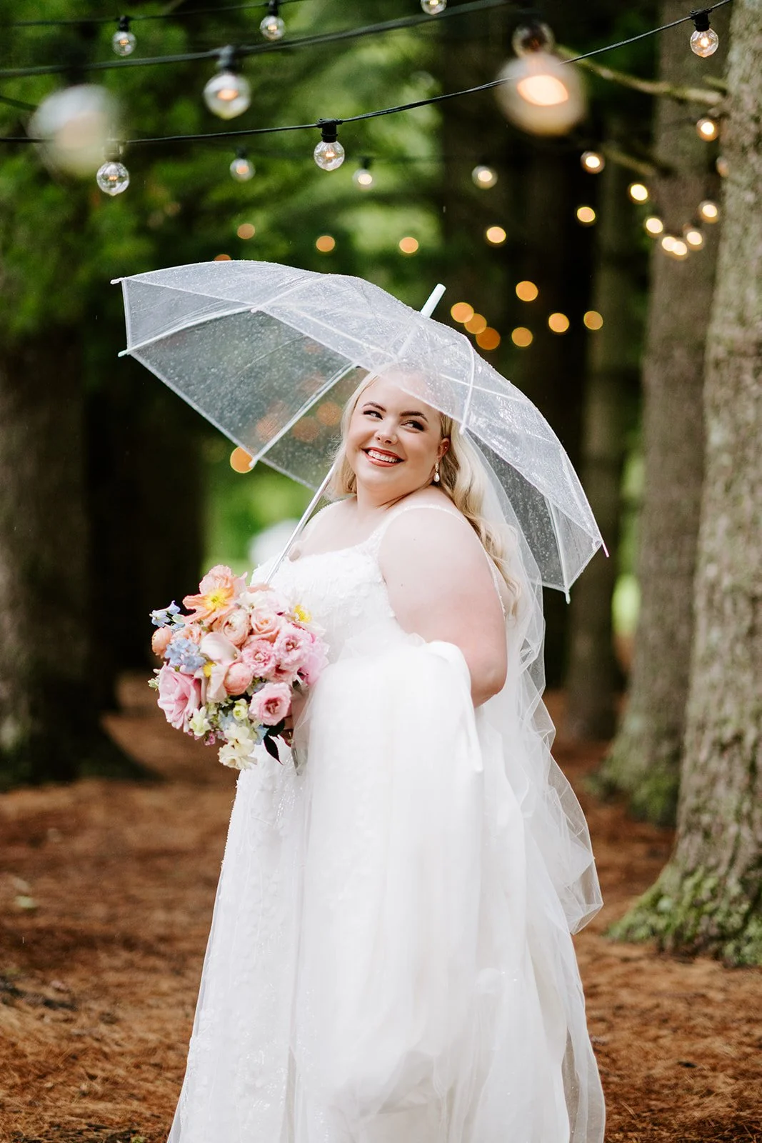 Bride with parasol and bouquet beneath string lights in the pines, florals by Hydrangea Bloom, photographed by Karly Ellis Photography