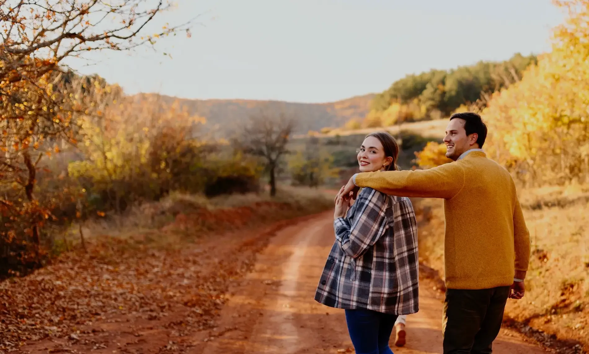 A couple walking together on a quiet country road in autumn, looking back and smiling