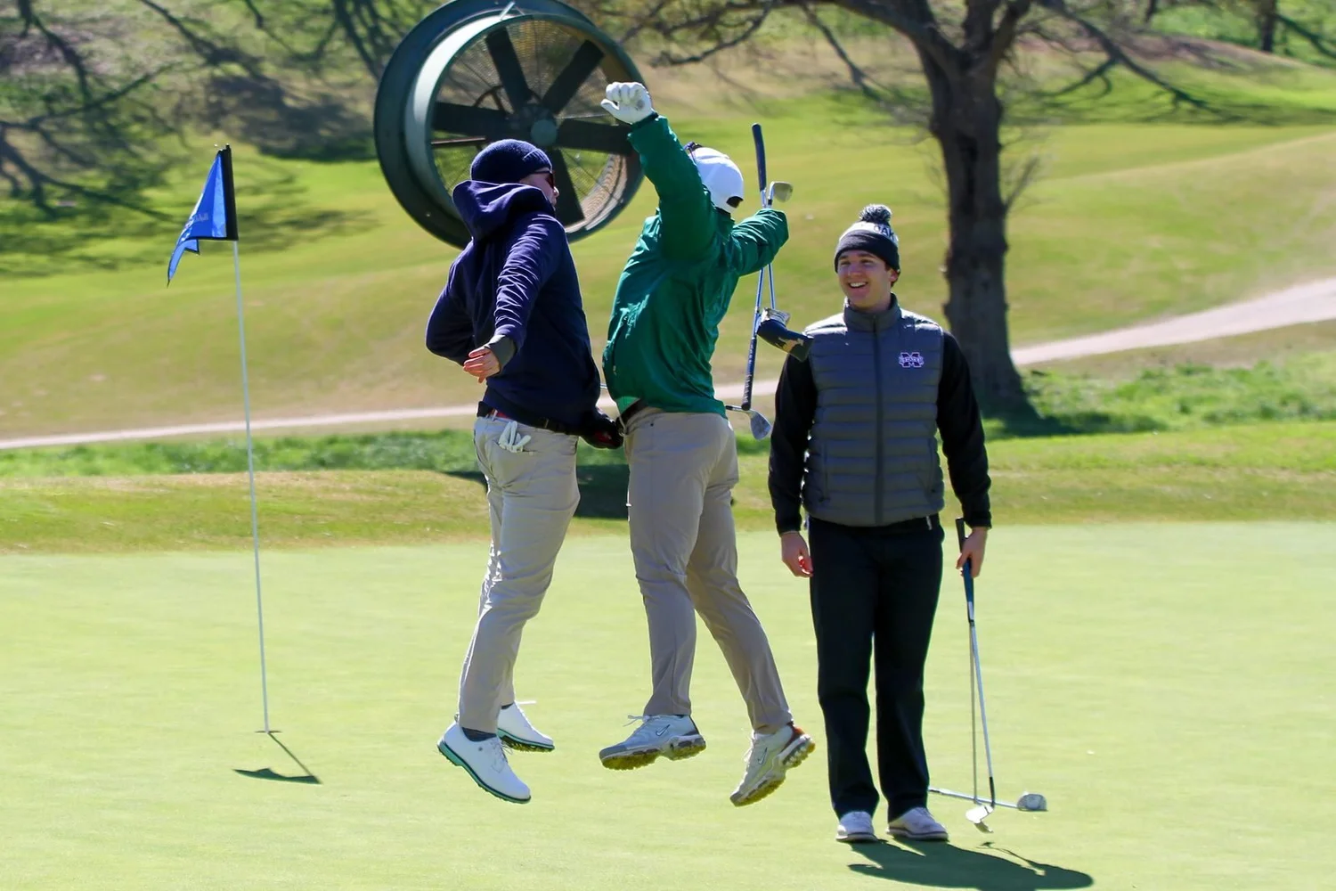 Two golfers jumping for a high five on the green
