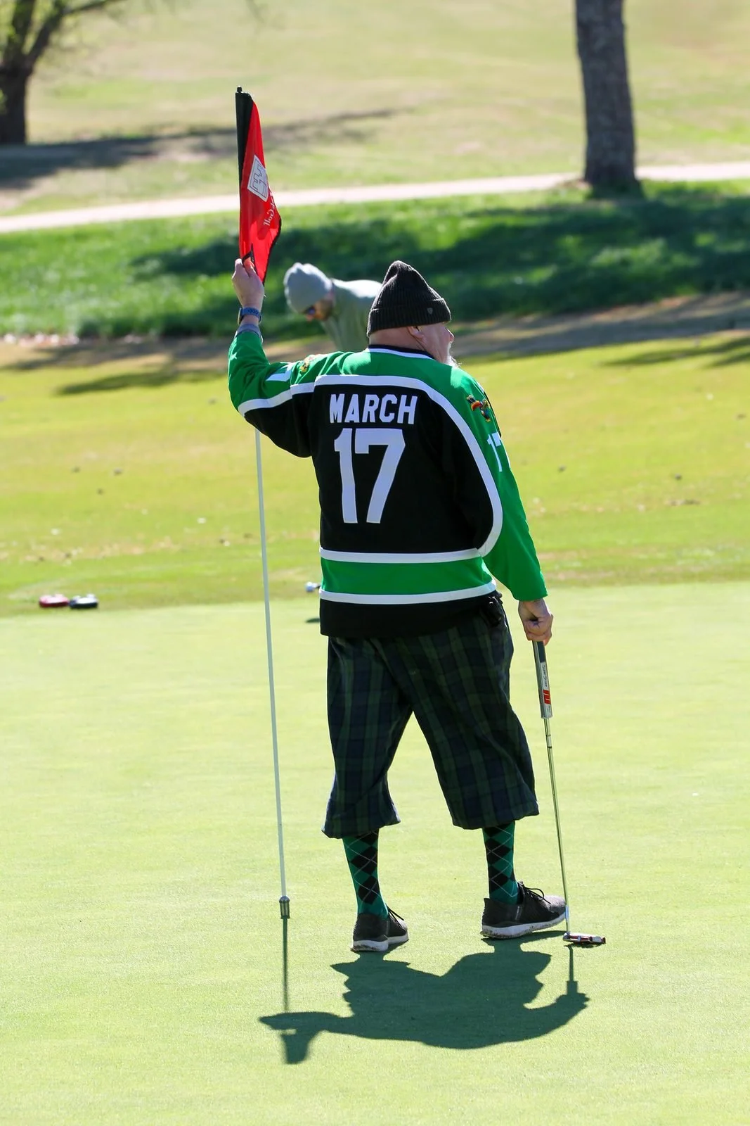 Golfer in a green jersey holding the flag