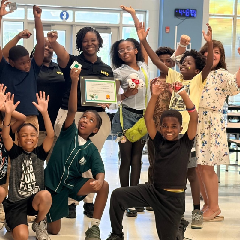 Students and teachers celebrating with raised hands at a Plastic to Purpose workshop award presentation