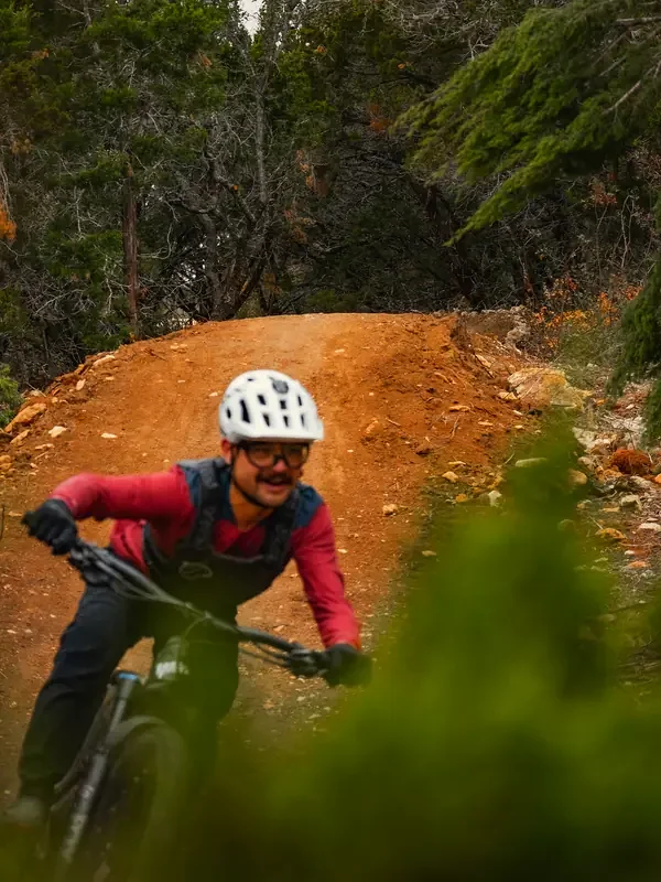 Rider in a white helmet driving out of a berm framed by cedar