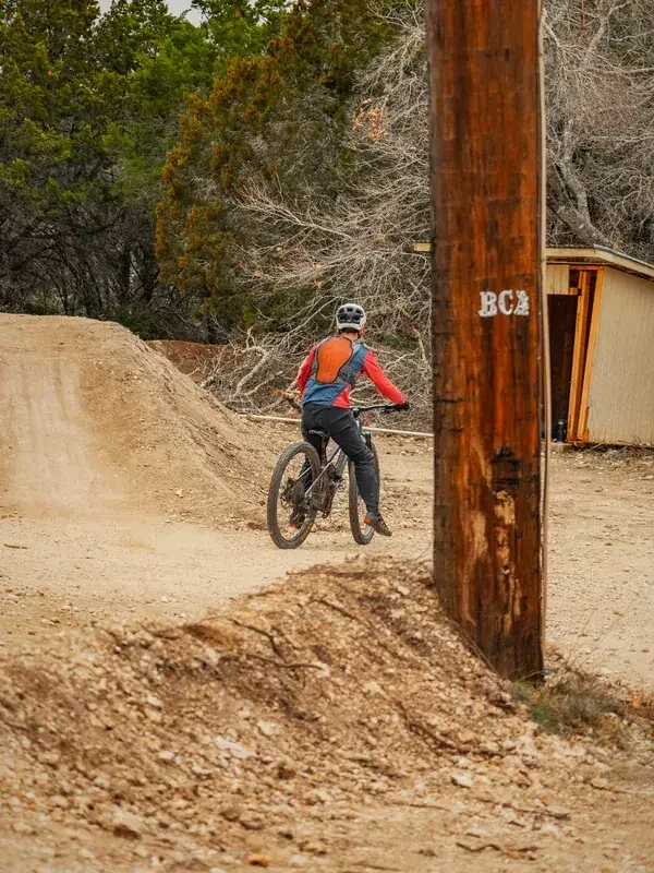 Rider rolling into a dirt jump line between the trees