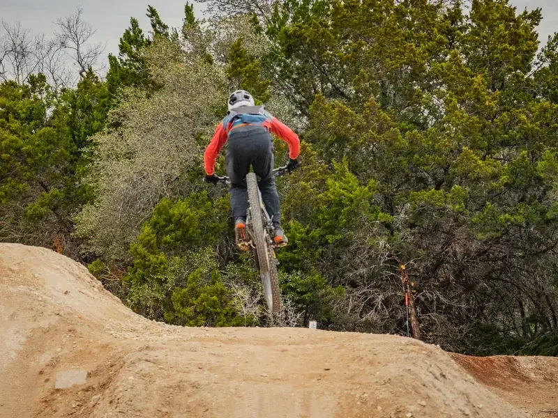 Rider clearing a roller on a hand-shaped dirt pump track lined with cedar