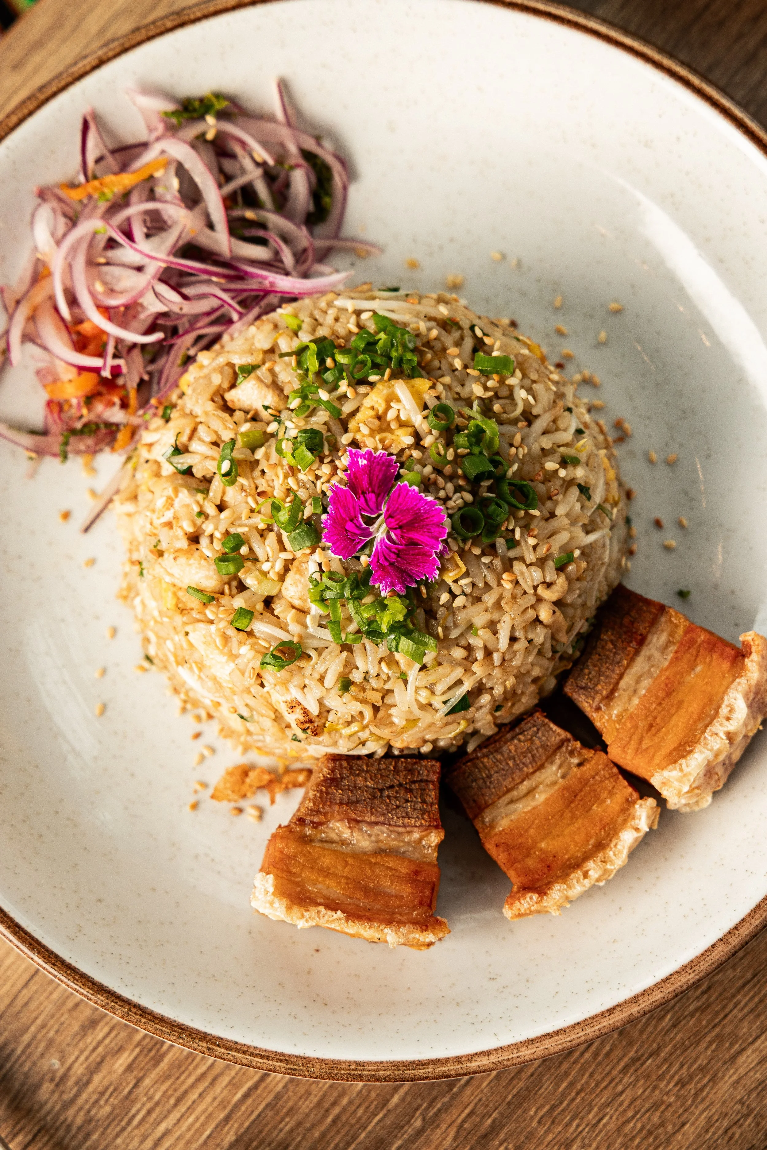 Fried rice topped with crispy pork, red onion and edible flowers at Enkai.
