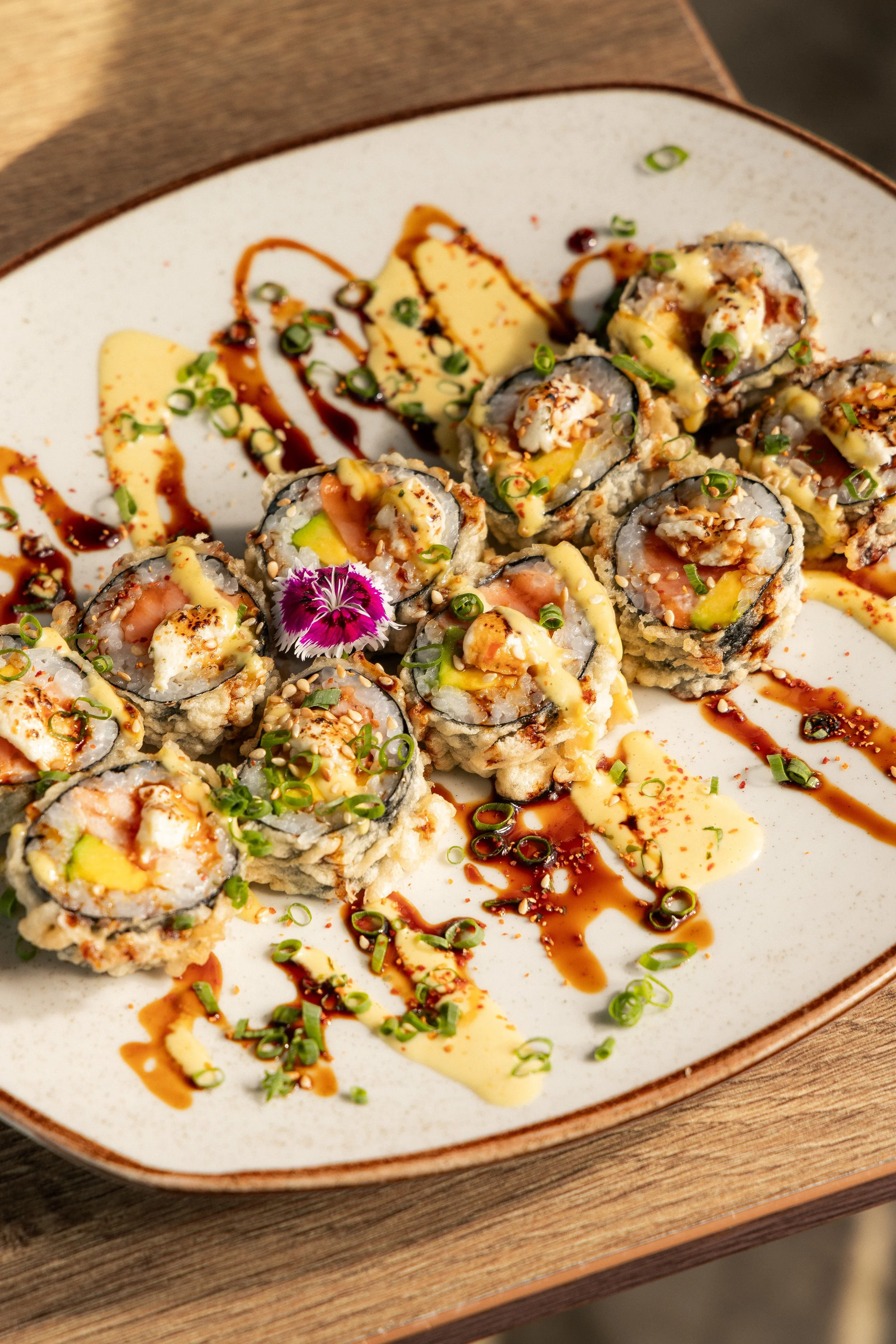 Colorful Enkai sushi rolls with avocado, sauces and edible flowers.