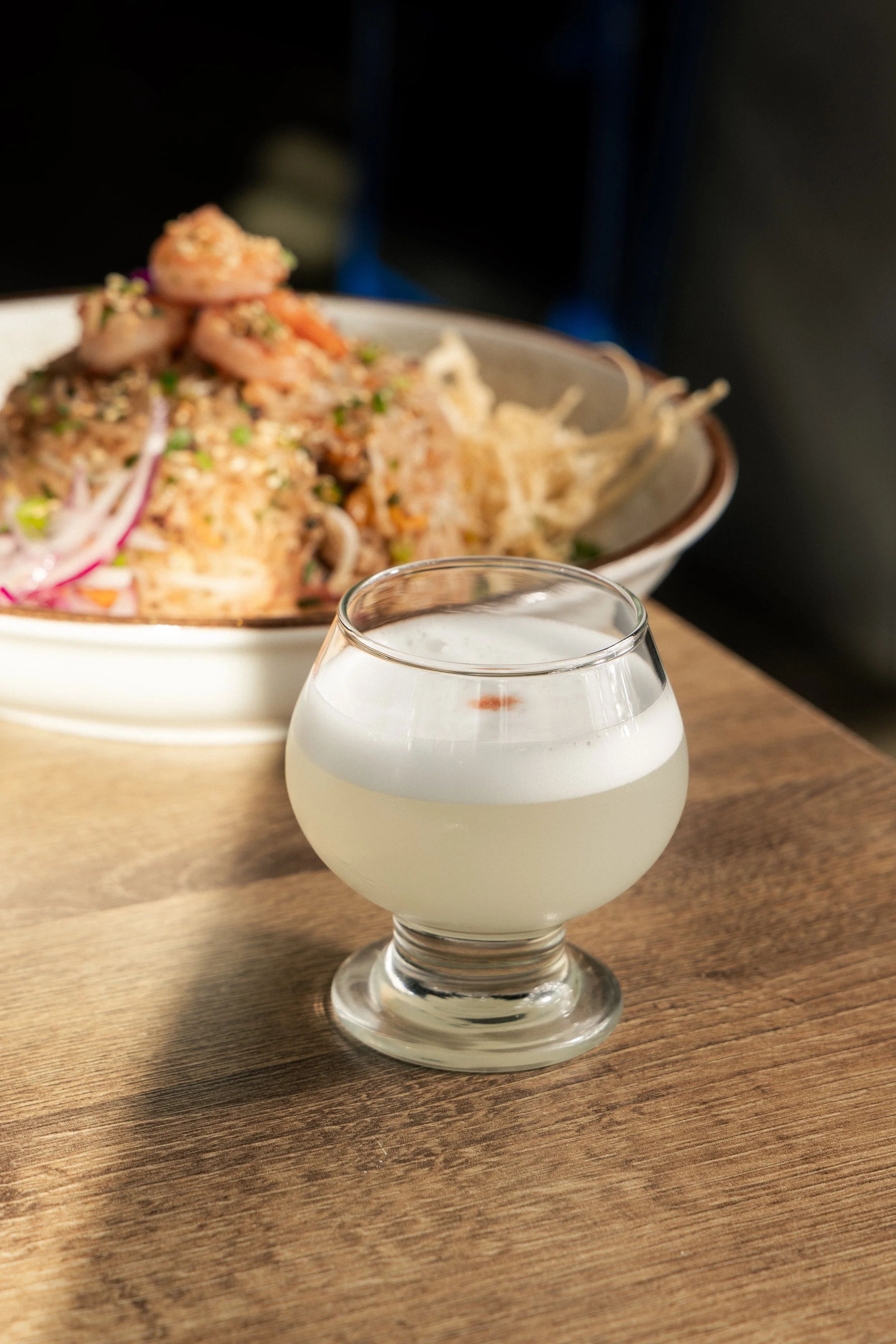 Pisco Sour served beside Enkai dishes on a restaurant table.