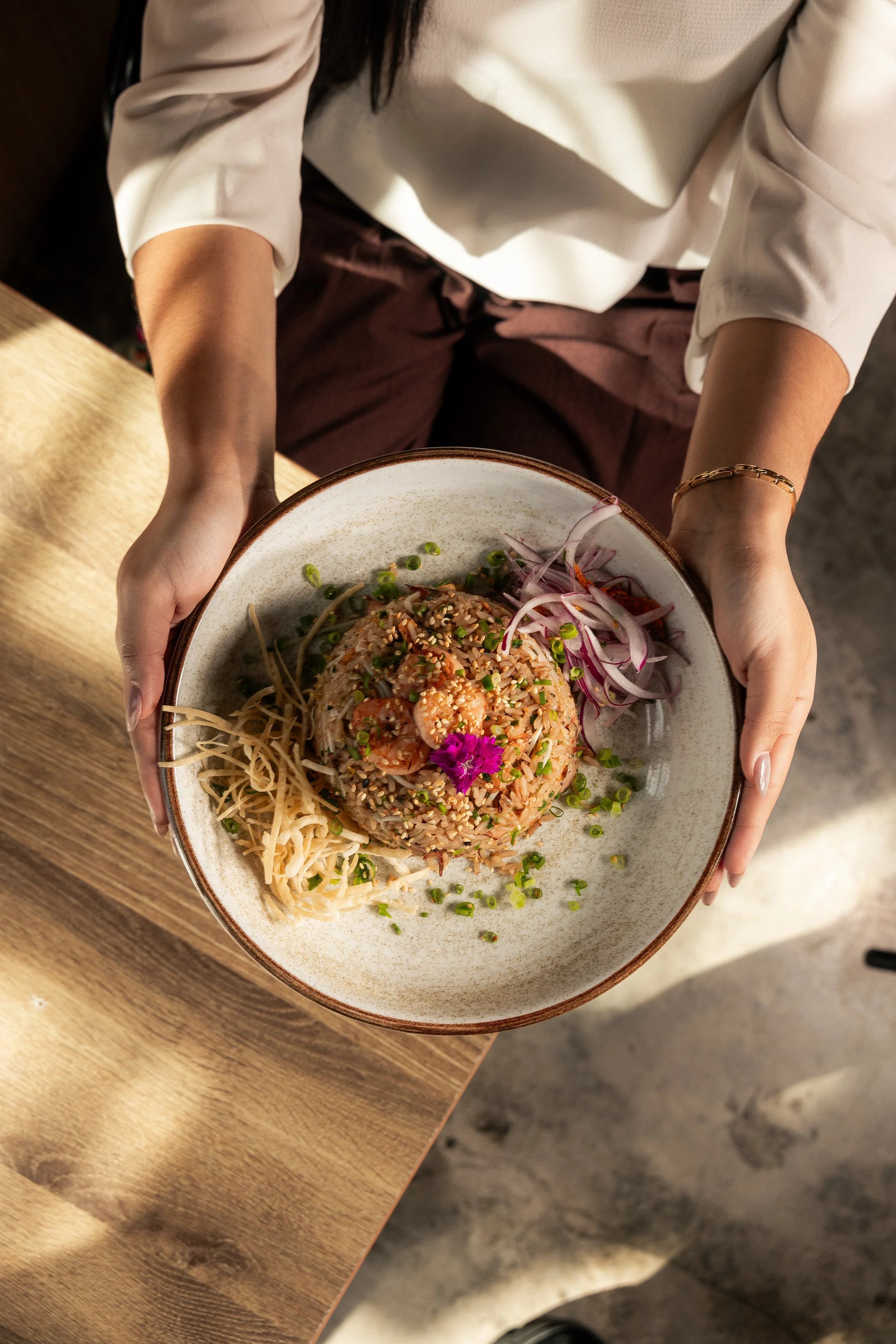 Server presenting Enkai fried rice topped with shrimp and edible flowers.