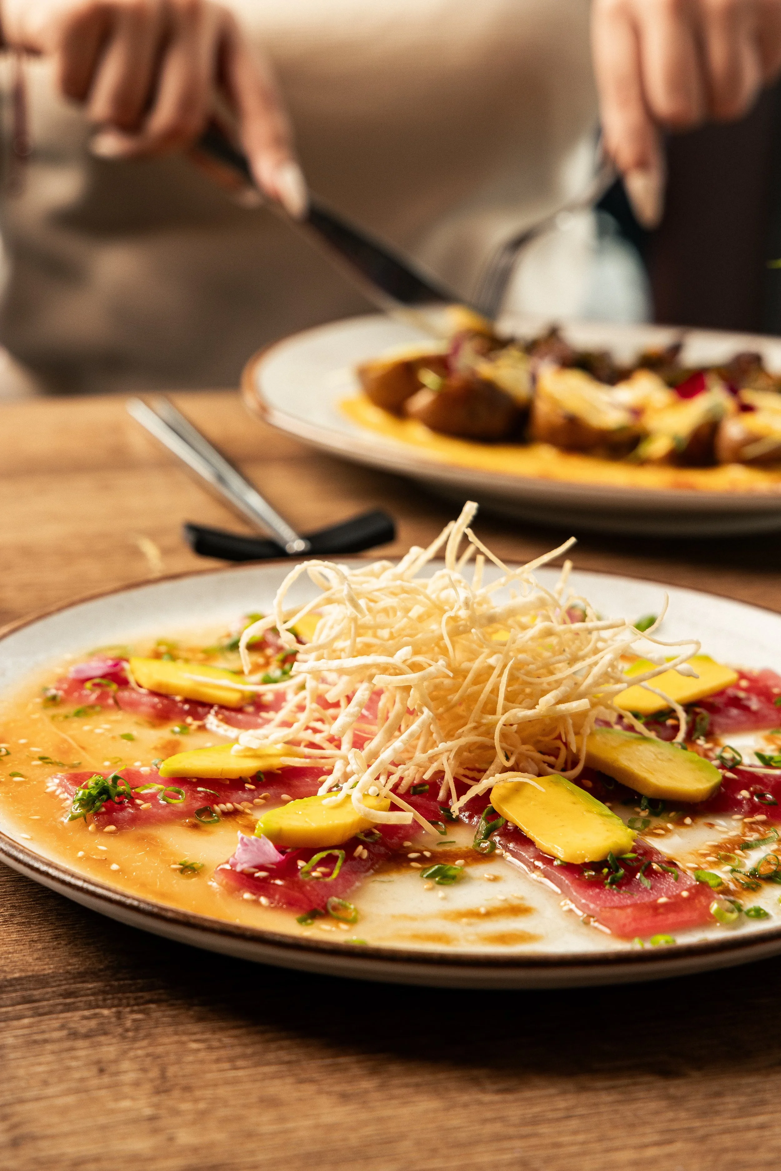 Nikkei tiradito with sliced fish, avocado, red onion and crispy potato strips.
