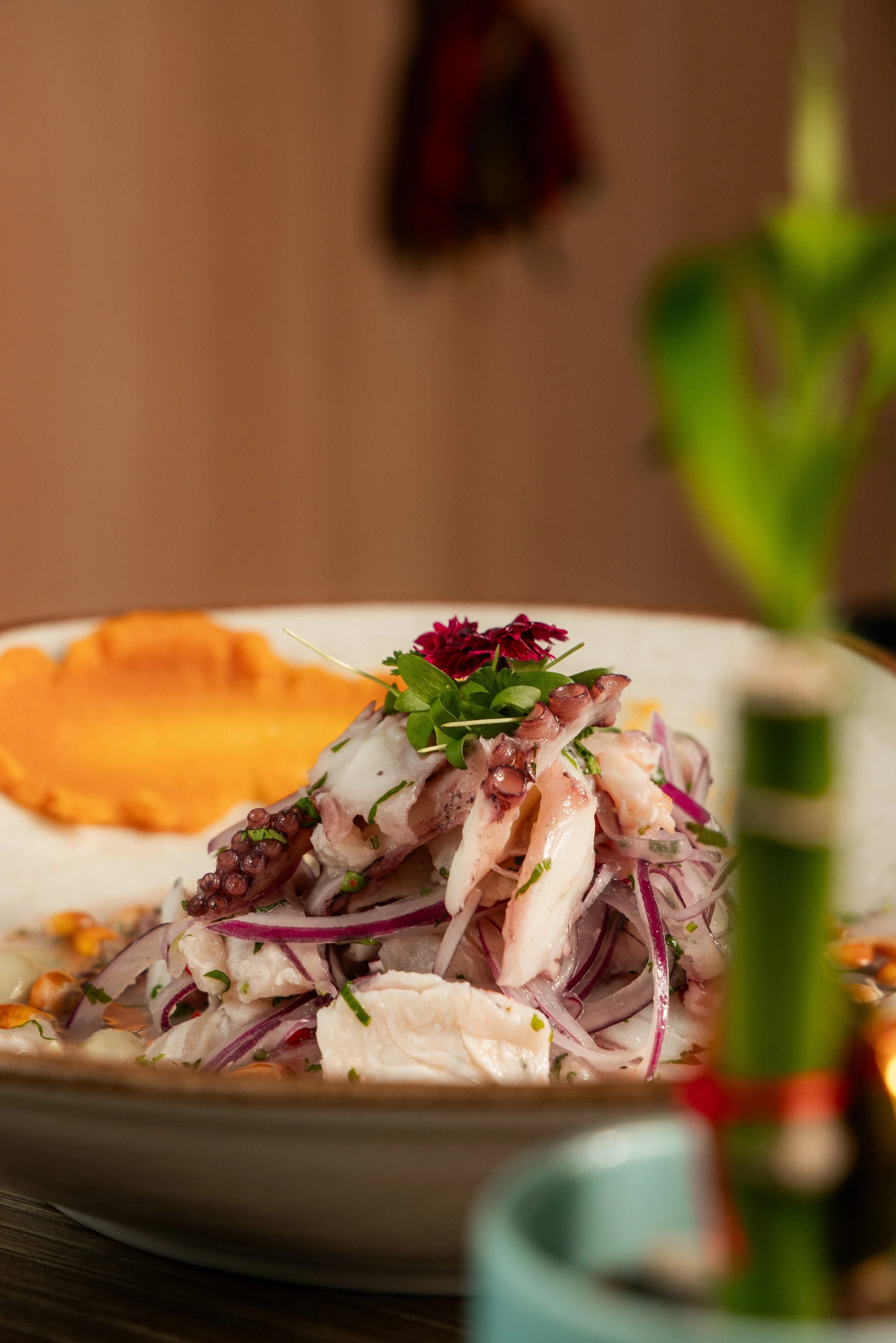Close view of a ceviche-style fish dish with red onion and edible flowers at Enkai.