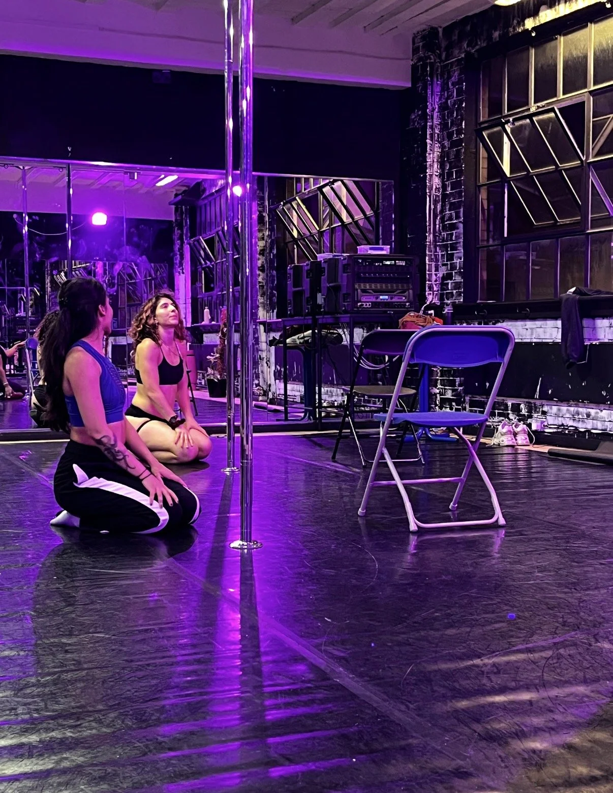 Two participants kneeling beside a pole in a purple-lit mirrored studio