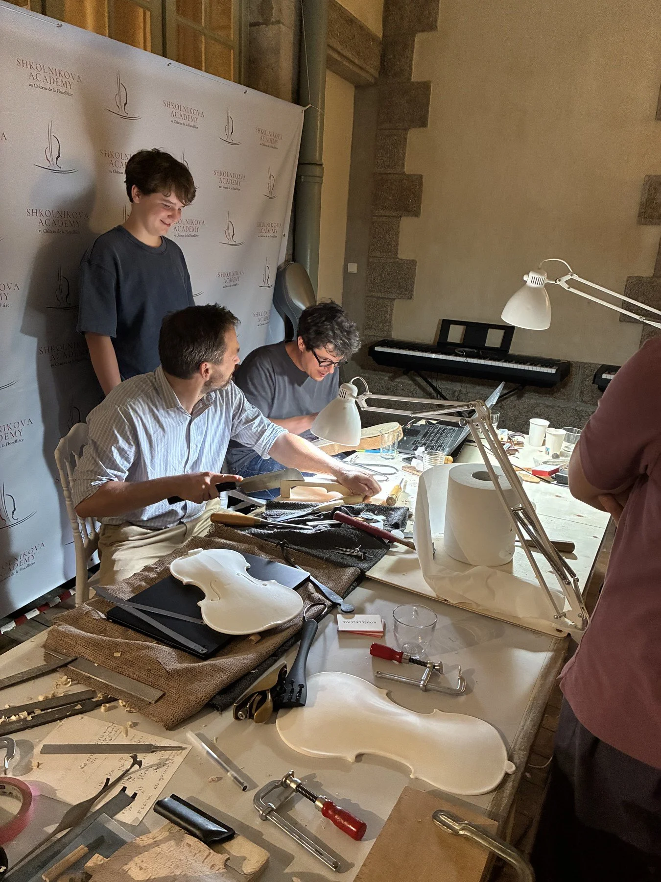 Luthiers working on the violin copy as an Academy participant looks on
