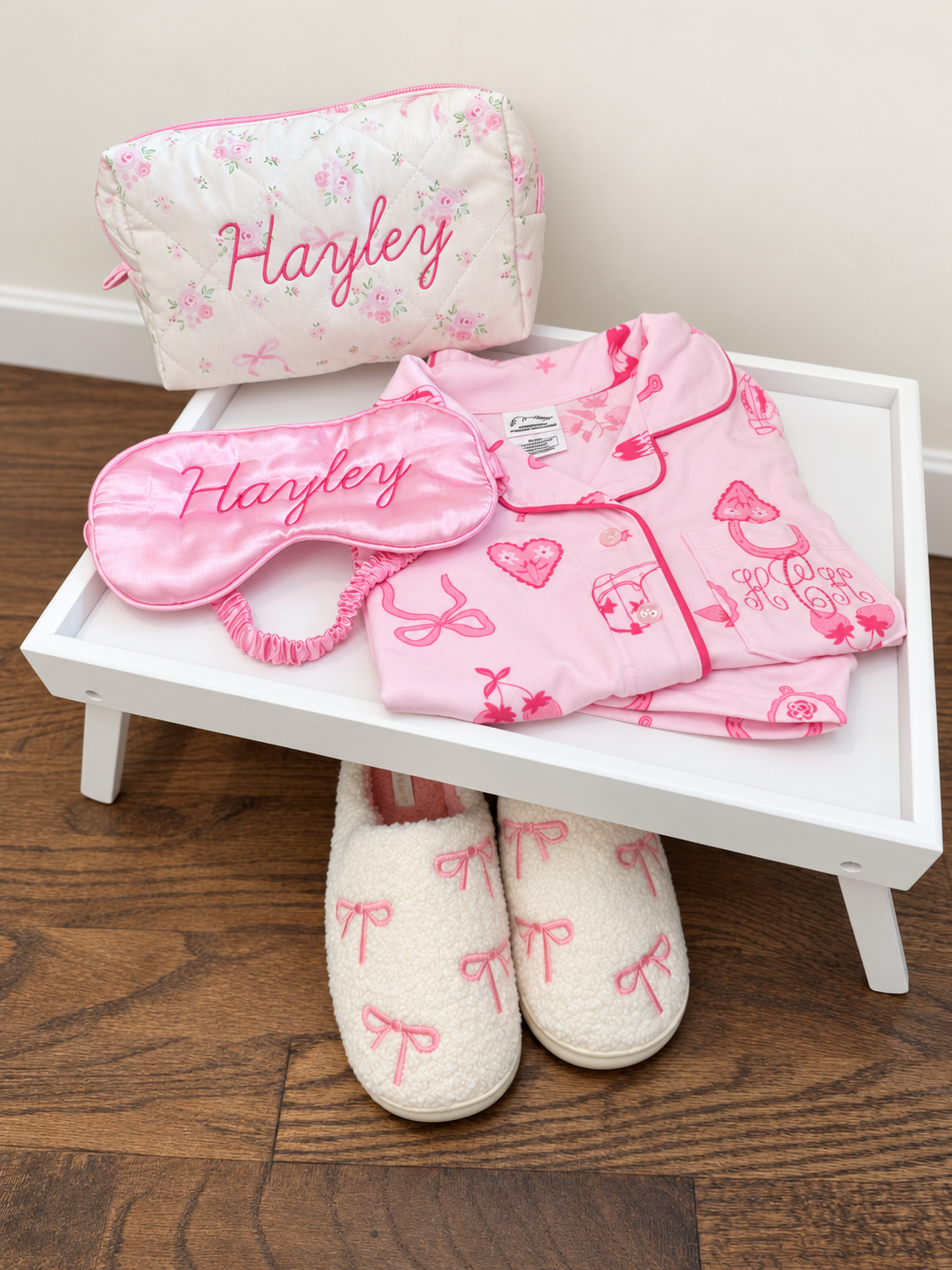 Personalized pink sleep mask, floral pouch and pajamas arranged on a white party tray