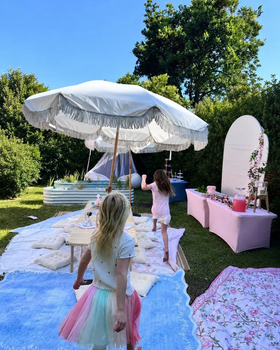 Children playing at a garden celebration with a fringed parasol and pastel picnic setting