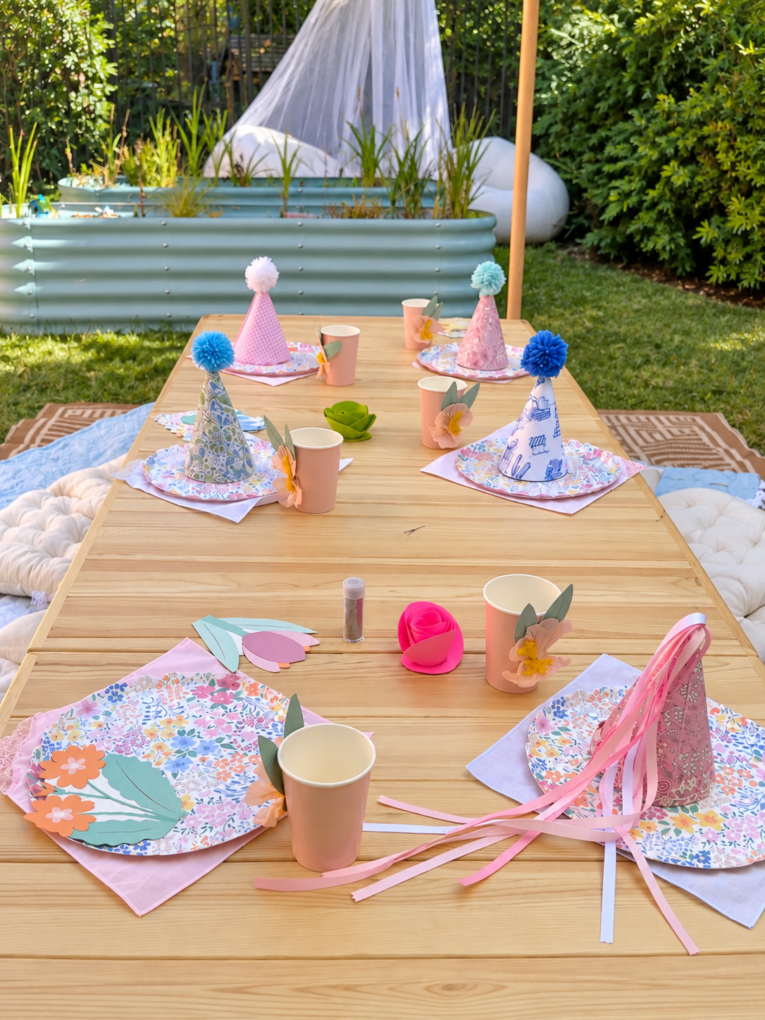 A garden picnic table set with pastel party hats, floral plates and cushions