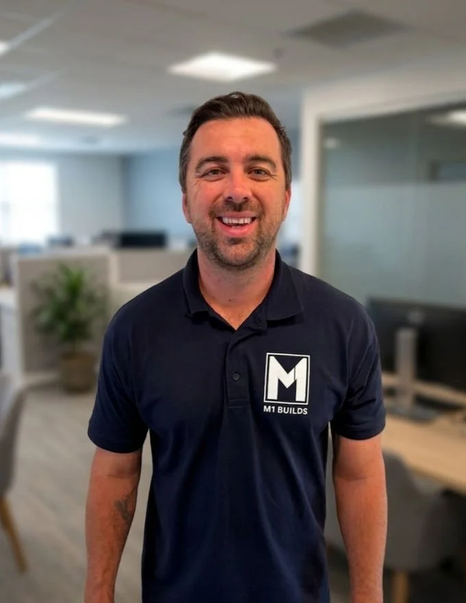 Man, M1 BUILDS, blue polo shirt, arm tattoos, office setting, construction, building.
