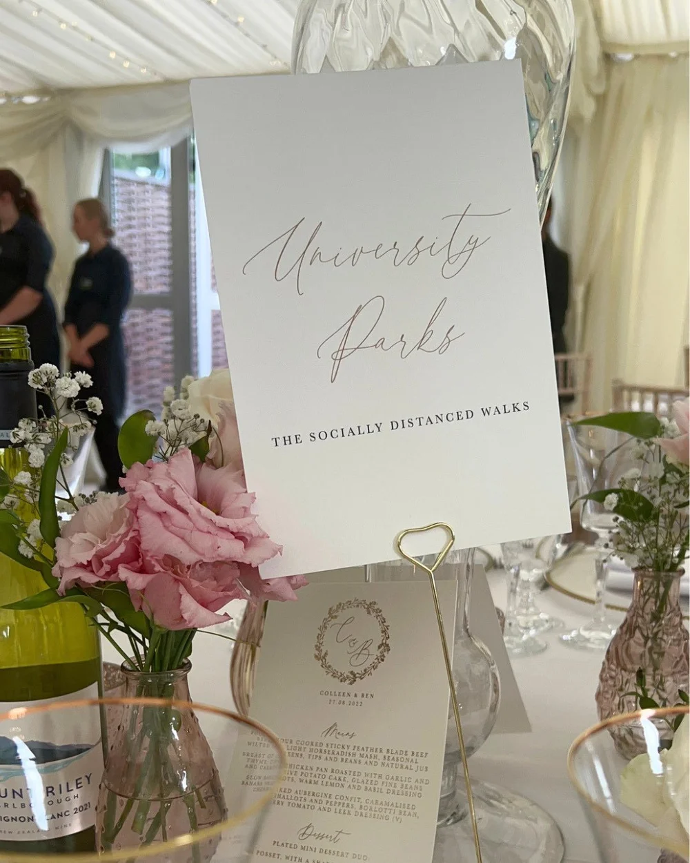 A wedding table with pink flowers, a University Parks table sign and Ben and Colleen’s menu.