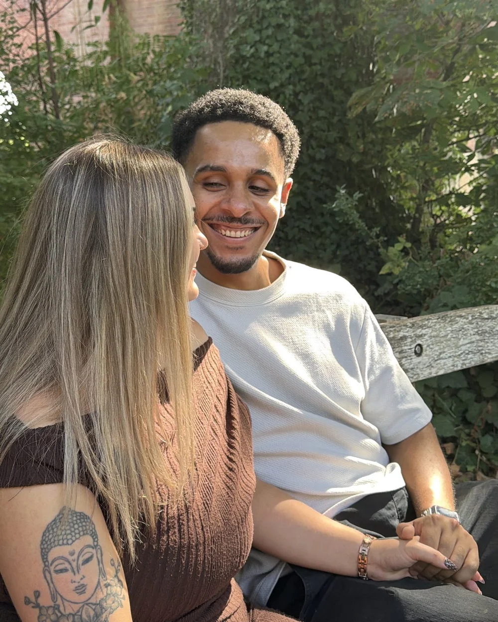 Josh smiling at Jas as they sit together on a riverside bench.