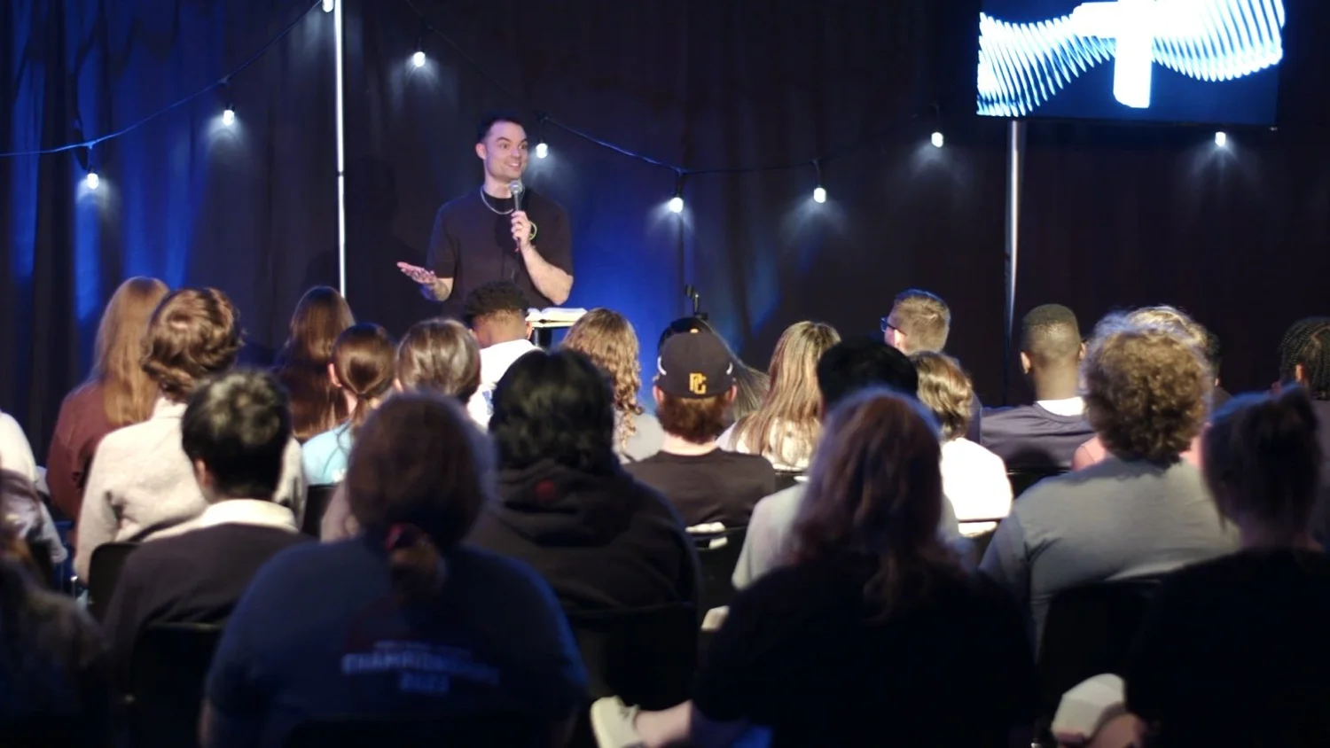 Seth holding a microphone and speaking to an audience seated close to the stage