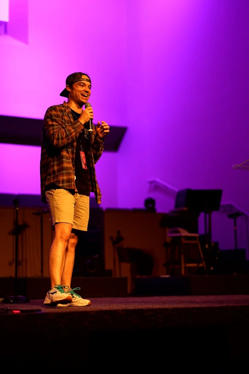 Seth smiling while speaking with a microphone on a purple-lit stage
