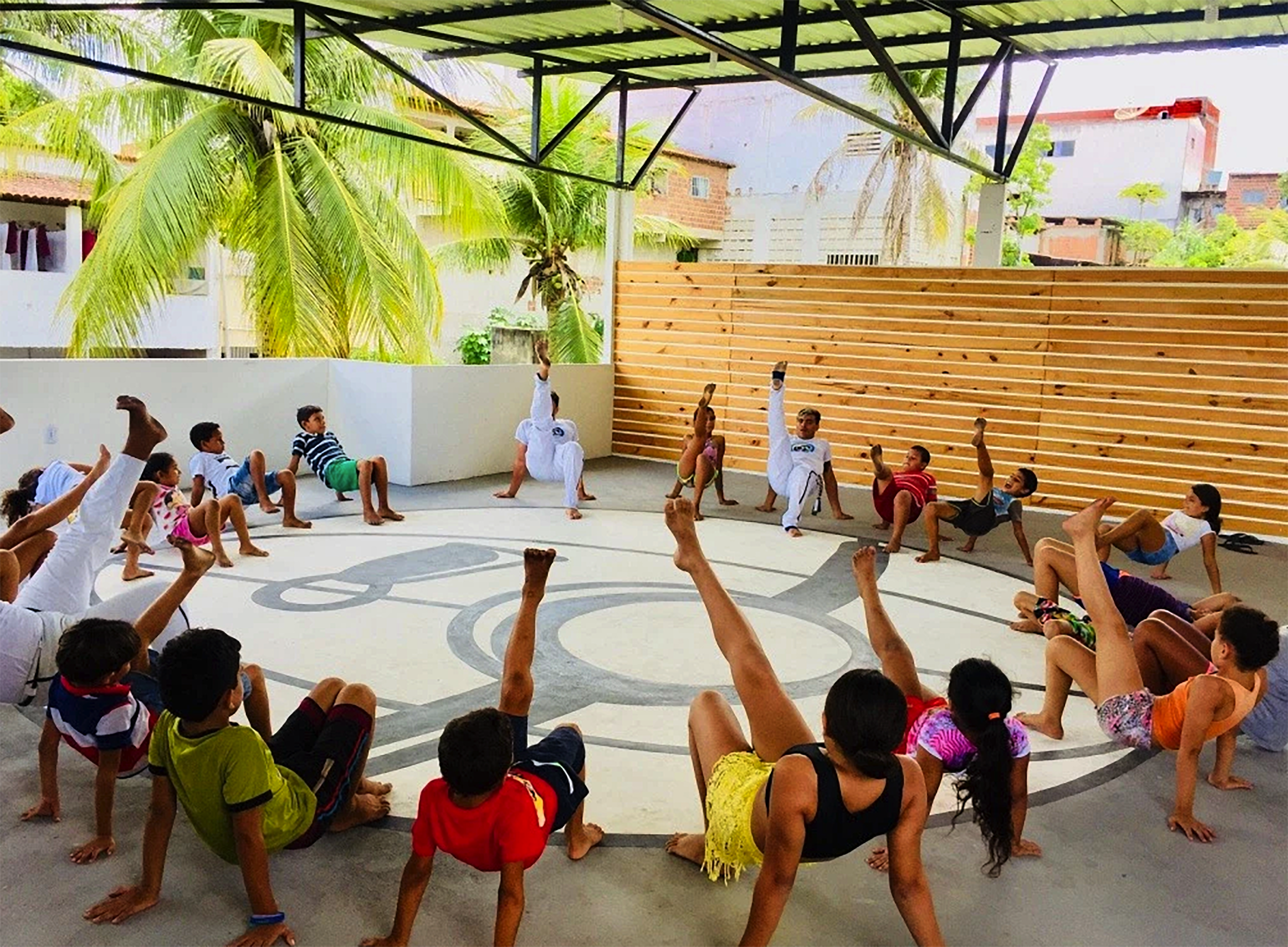 Kinder bilden beim Capoeira-Training einen Kreis; in der Mitte wird eine Bewegung vorgeführt.