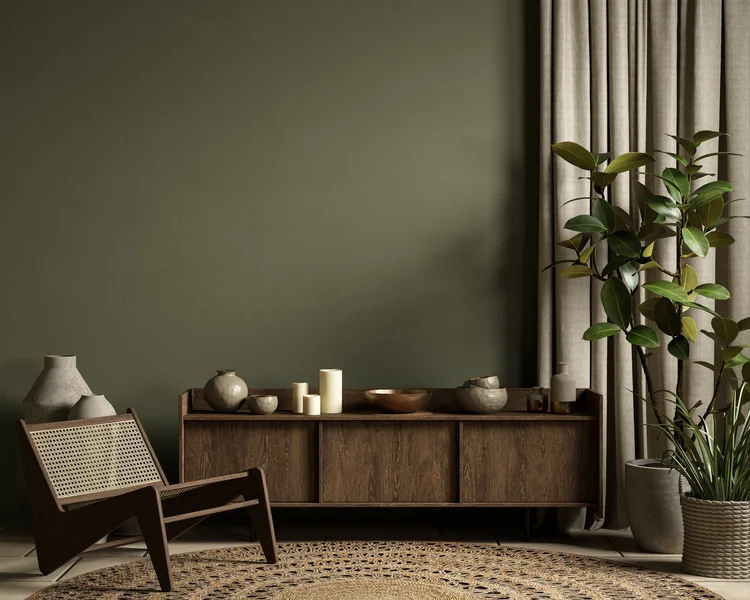 A room with deep olive green walls, a dark wood sideboard, a cane lounge chair and linen curtains