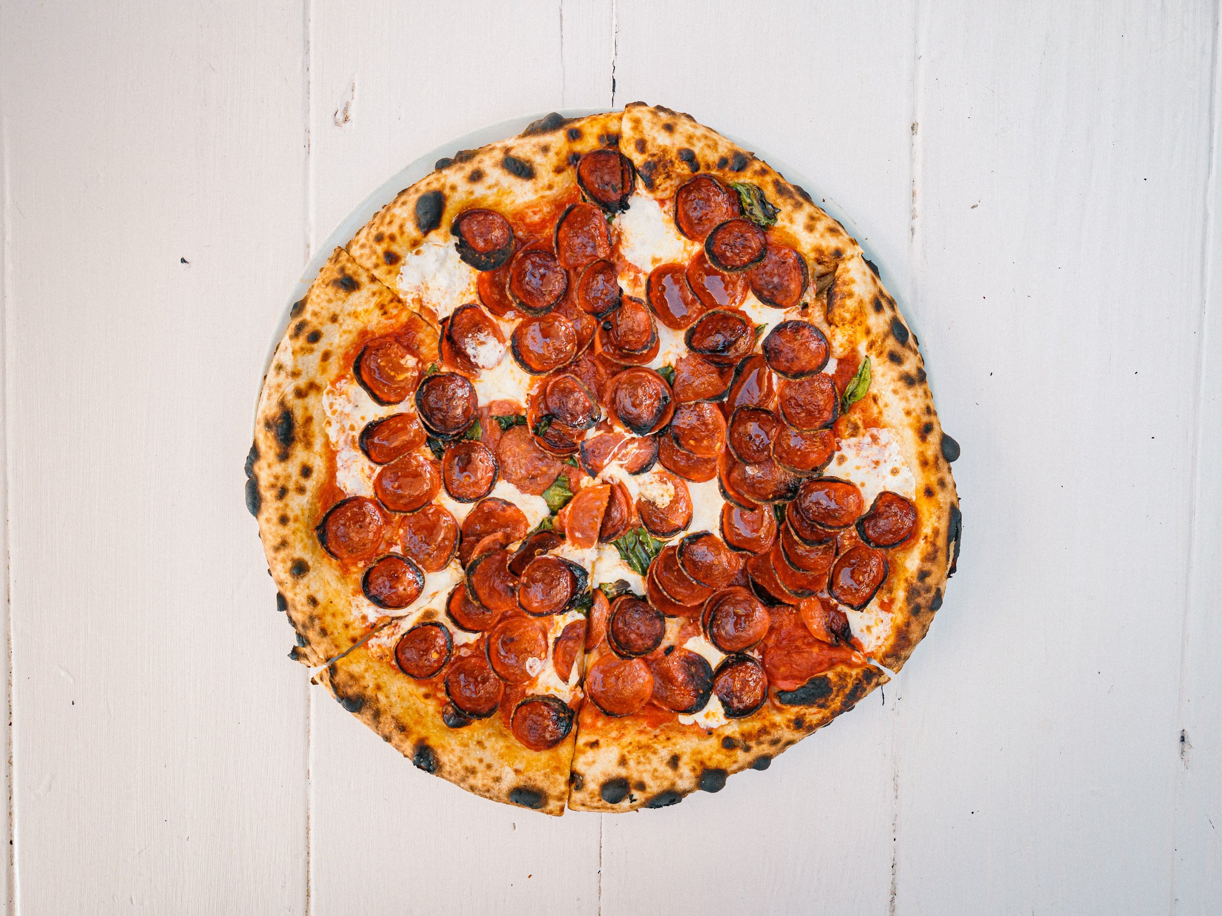 A freshly baked sourdough Neapolitan pizza on a white table, featuring a crispy crust and vibrant toppings.
