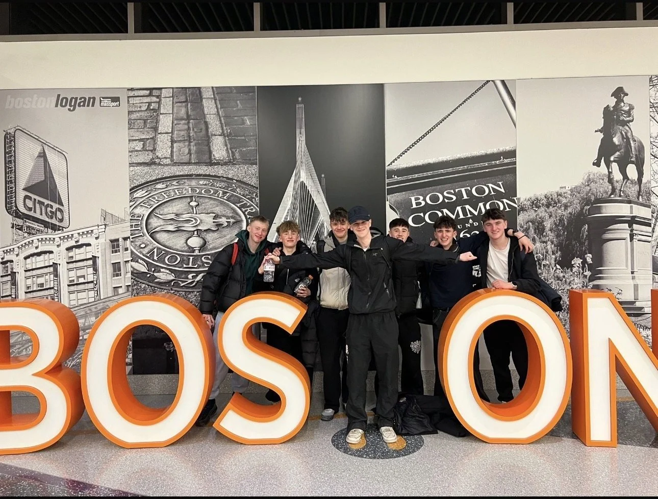 The group in front of the BOSTON sign at Logan Airport