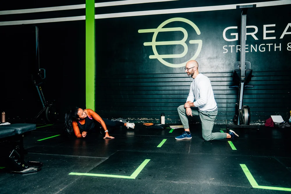 Eric kneeling beside a member on a mat to explain an exercise at GBSC.