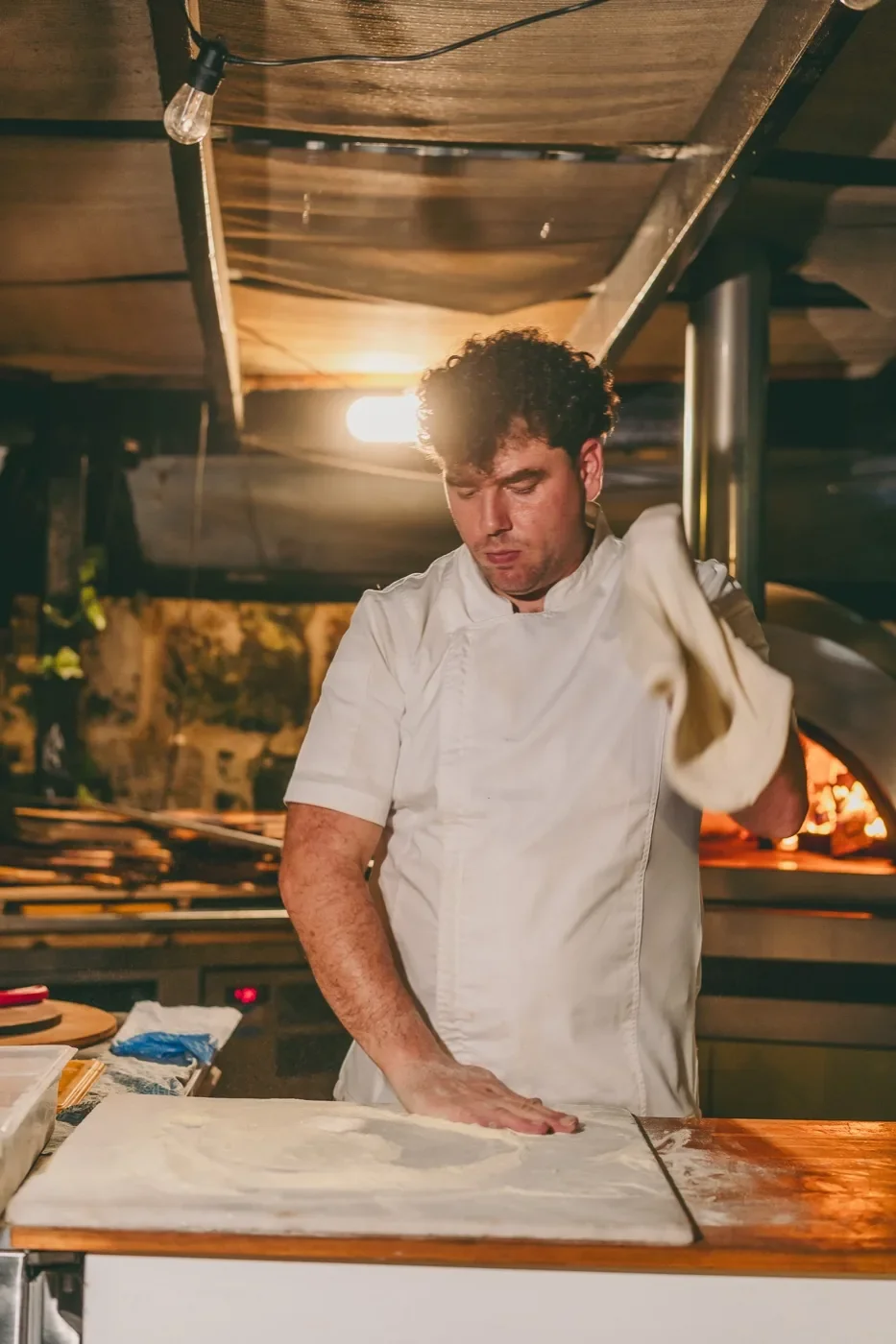 Chef stretching dough by the wood-fired oven