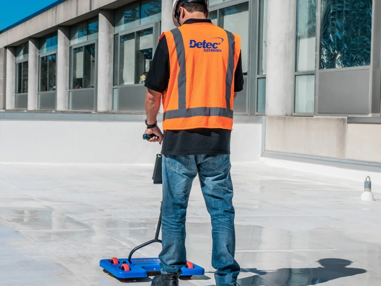 Technician scanning a white TPO roof membrane with DETEC Systems electronic leak detection equipment