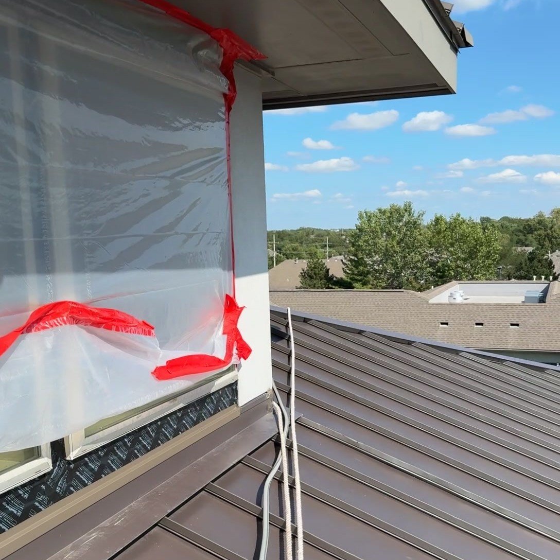 Window opening sealed with poly sheeting and red tape before a water test on a metal roof