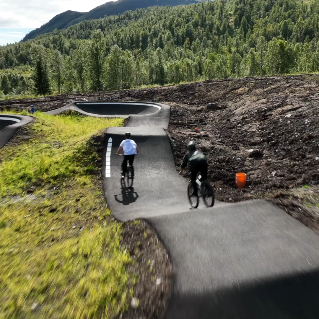 Cyclists on the pump track in Hodlekve with forest and mountains in the background