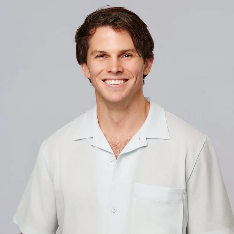 Young man in an open-collar white shirt, smiling on a light grey background. ATX Headshots, Austin.