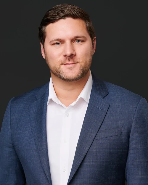 Man with short brown hair and a beard in a navy blazer and open white shirt, on a dark background. ATX Headshots, Austin.