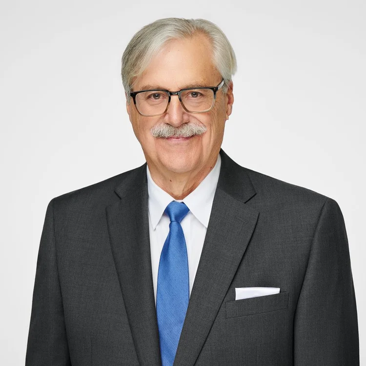Headshot of a smiling older man in glasses, a grey suit and blue tie, ATX Headshots