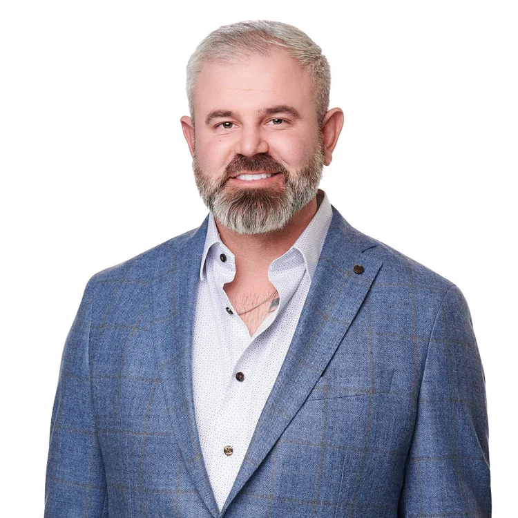 Headshot of a man in a blue-grey blazer and an open-collar white shirt, white background