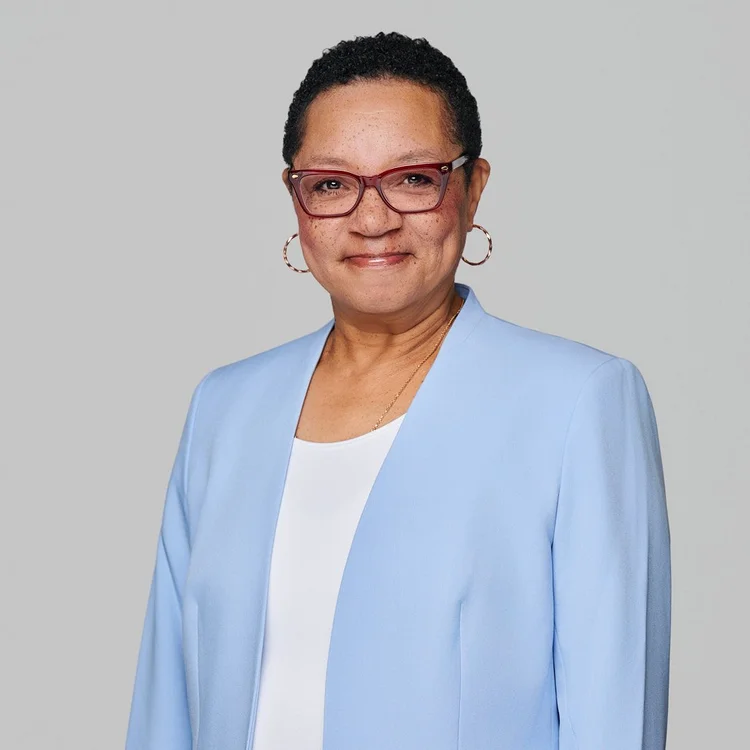 Headshot of a woman in glasses and a pale blue jacket over a white top, light grey background