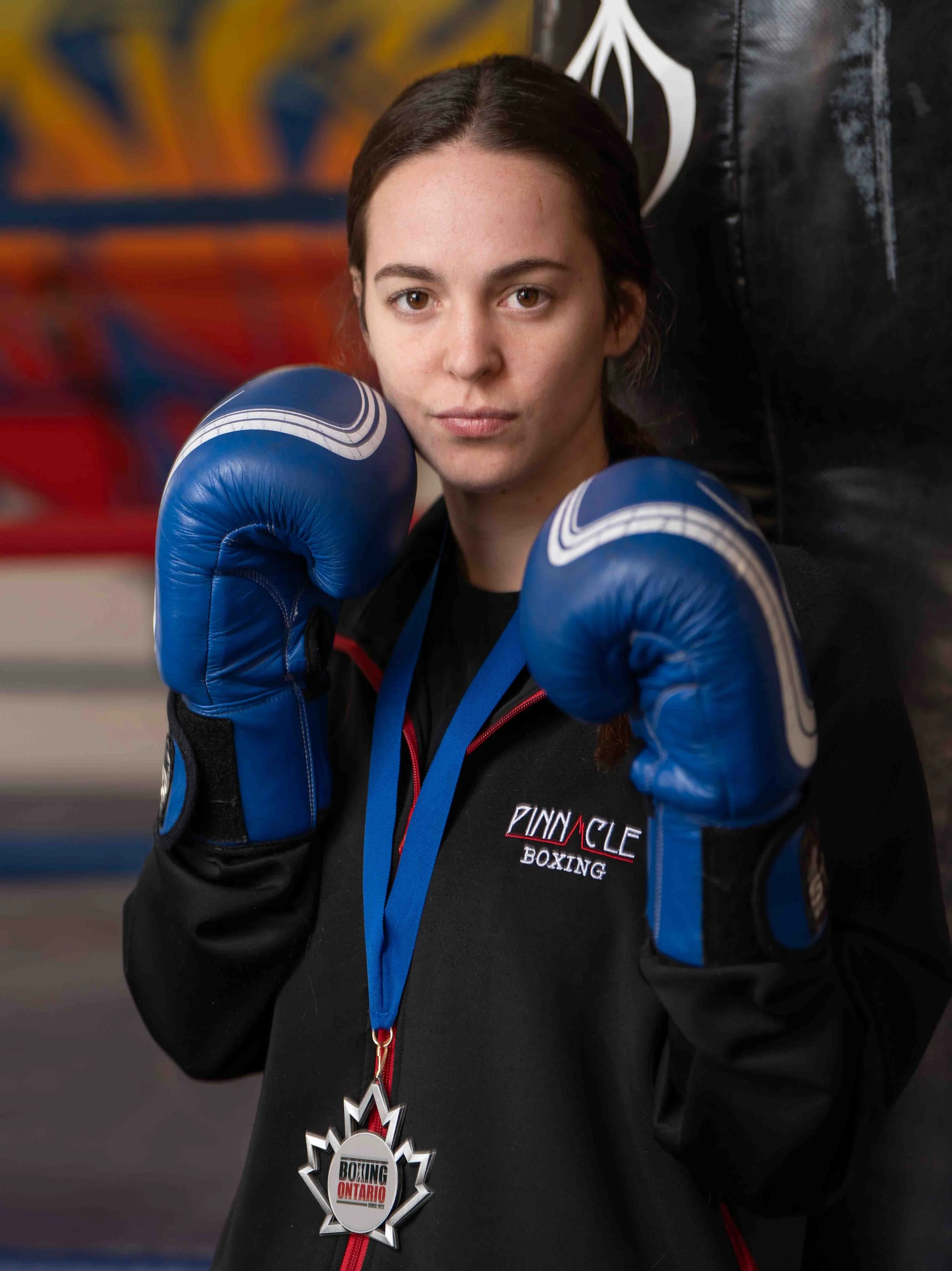 Makayla Johnson, silver medalist with Pinnacle Boxing Belleville, photographed after her fight wearing blue gloves and her Boxing Ontario medal.