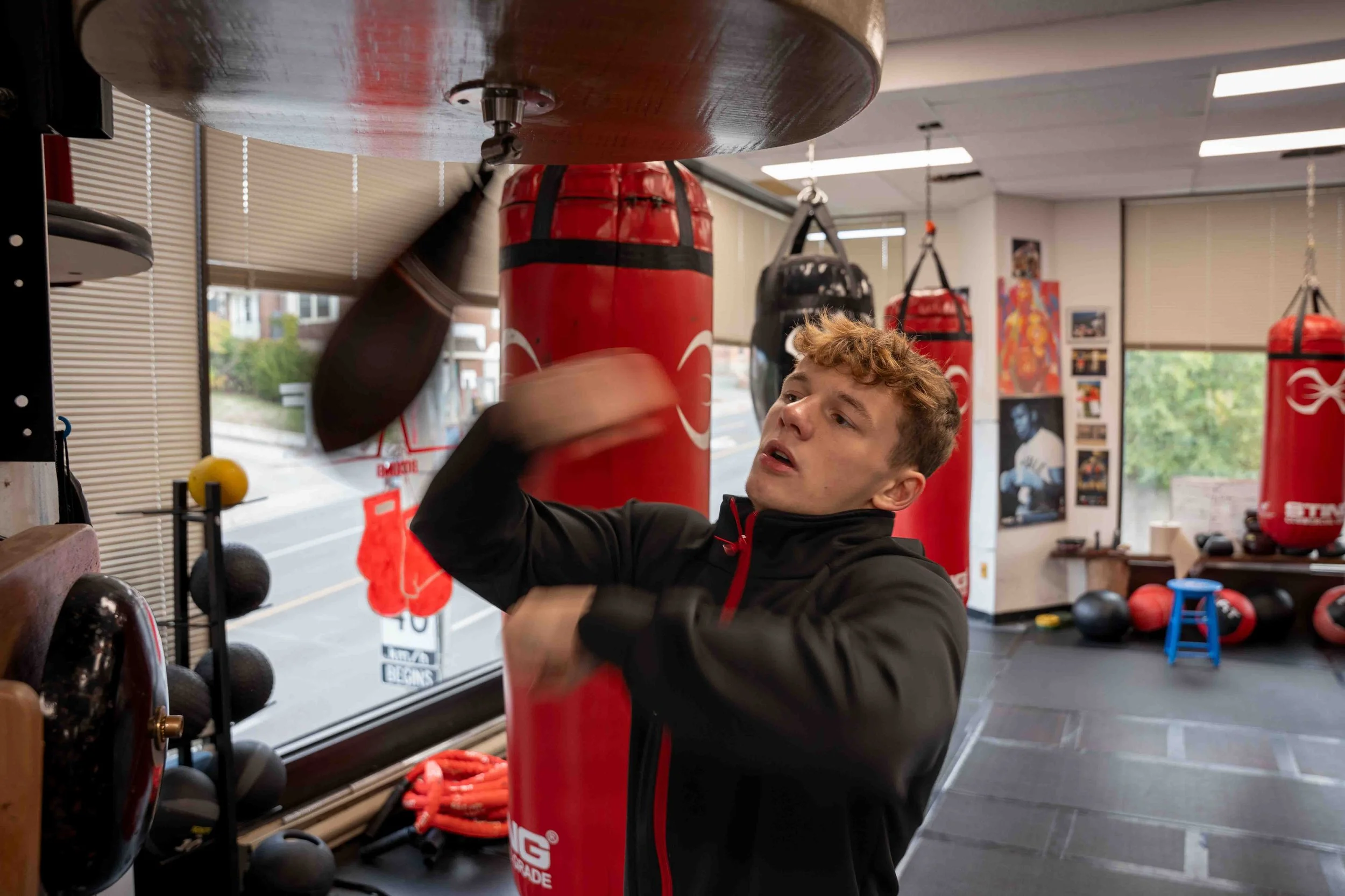 Action shot inside Pinnacle Boxing Belleville gym as a boxer throws punches on the bag under soft, directional light during training.