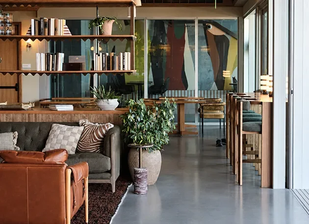 Lounge with built-in bookshelves, a leather sofa and planters beside full height glazing.