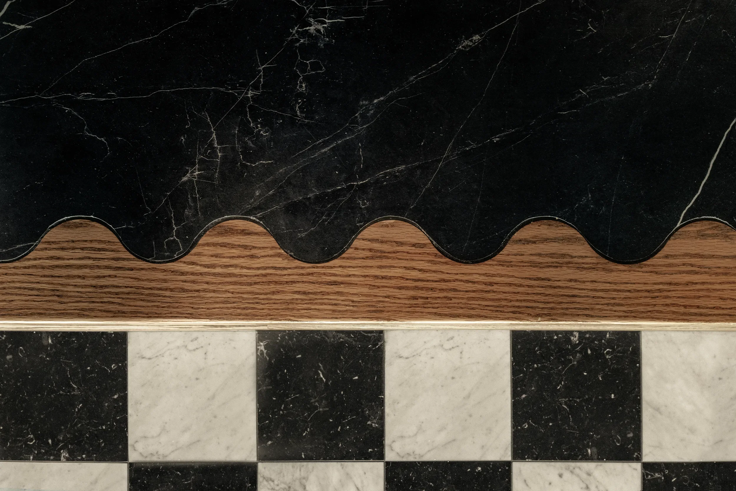 Detail of a scalloped black stone edge over white oak, above a checkered marble floor
