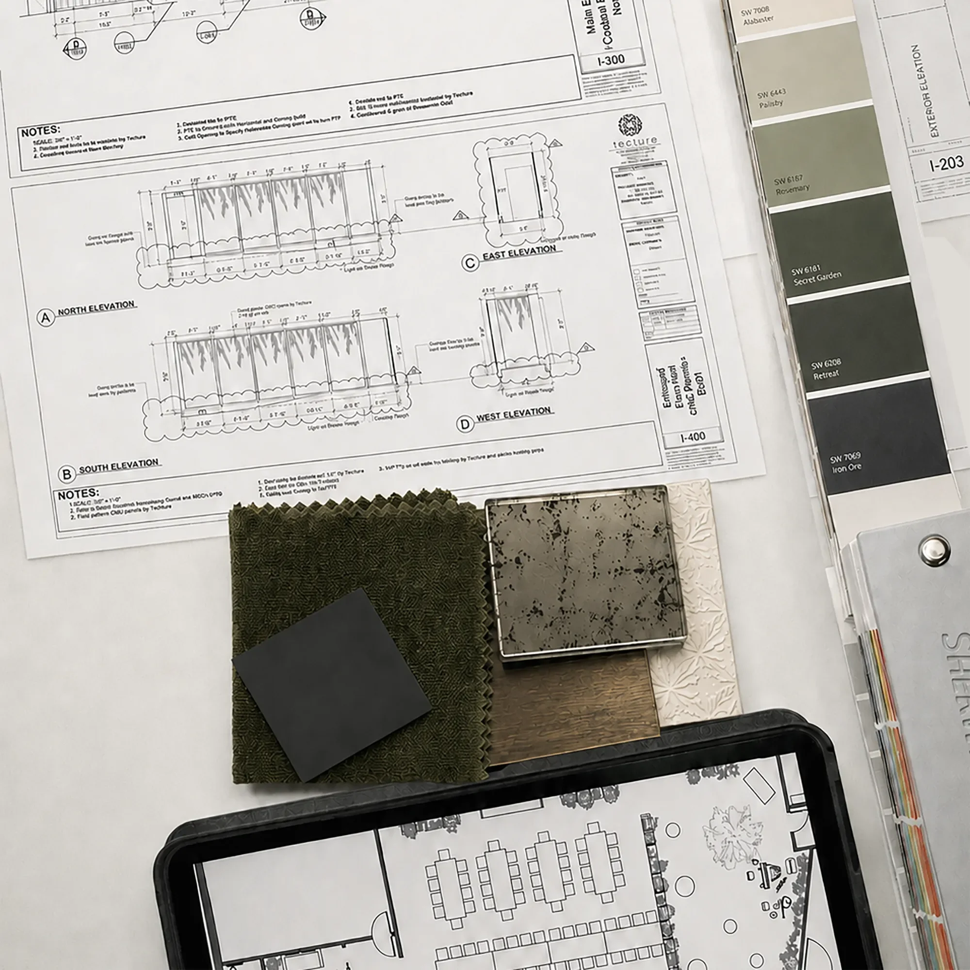 Elevation drawings on paper and tablet beside green textile and dark stone finish samples