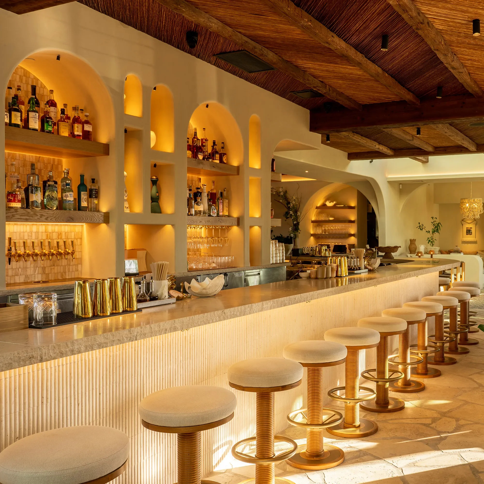 Fluted travertine bar front and backlit arched liquor niches at By The Sea in Coronado