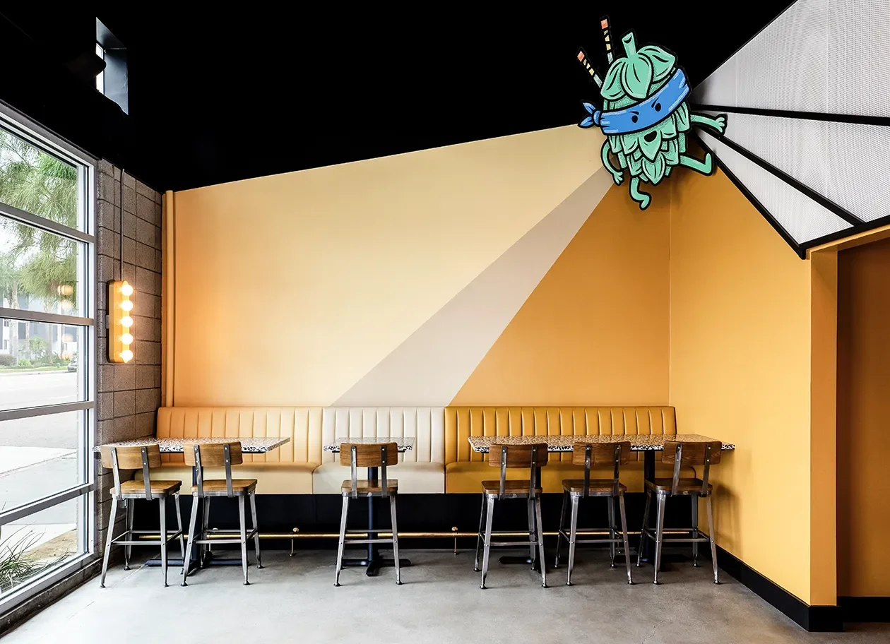 Angled wall graphic and painted character mural above banquette seating in a taproom interior.